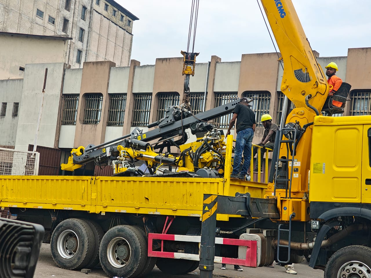 Des intervenants accompagnent la manutention d’un équipement sur un camion équipé d’une grue.