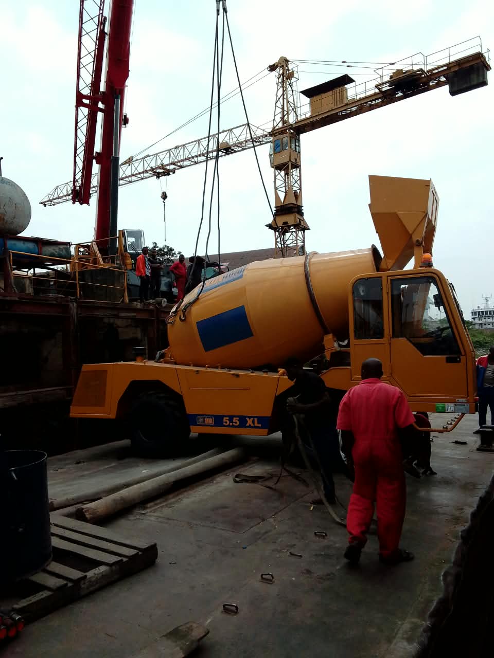 Une bétonnière automotrice est prise en charge par une grue dans une zone de chargement.