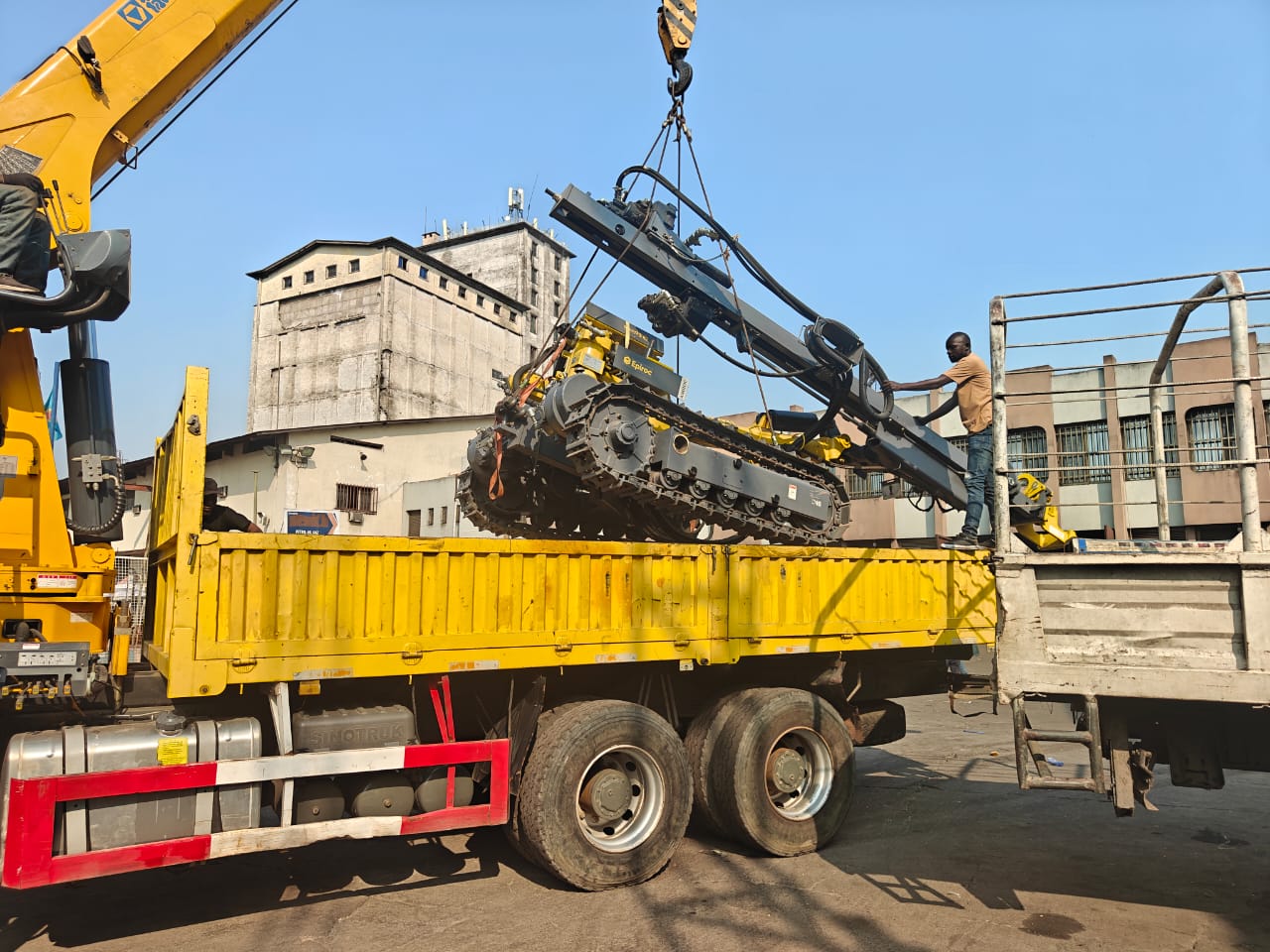 Un engin de forage sur chenilles est soulevé au-dessus de la caisse d’un camion.